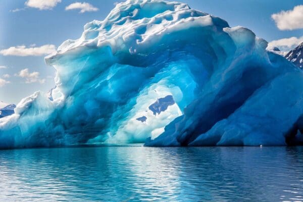 Blue iceberg arch over calm water.