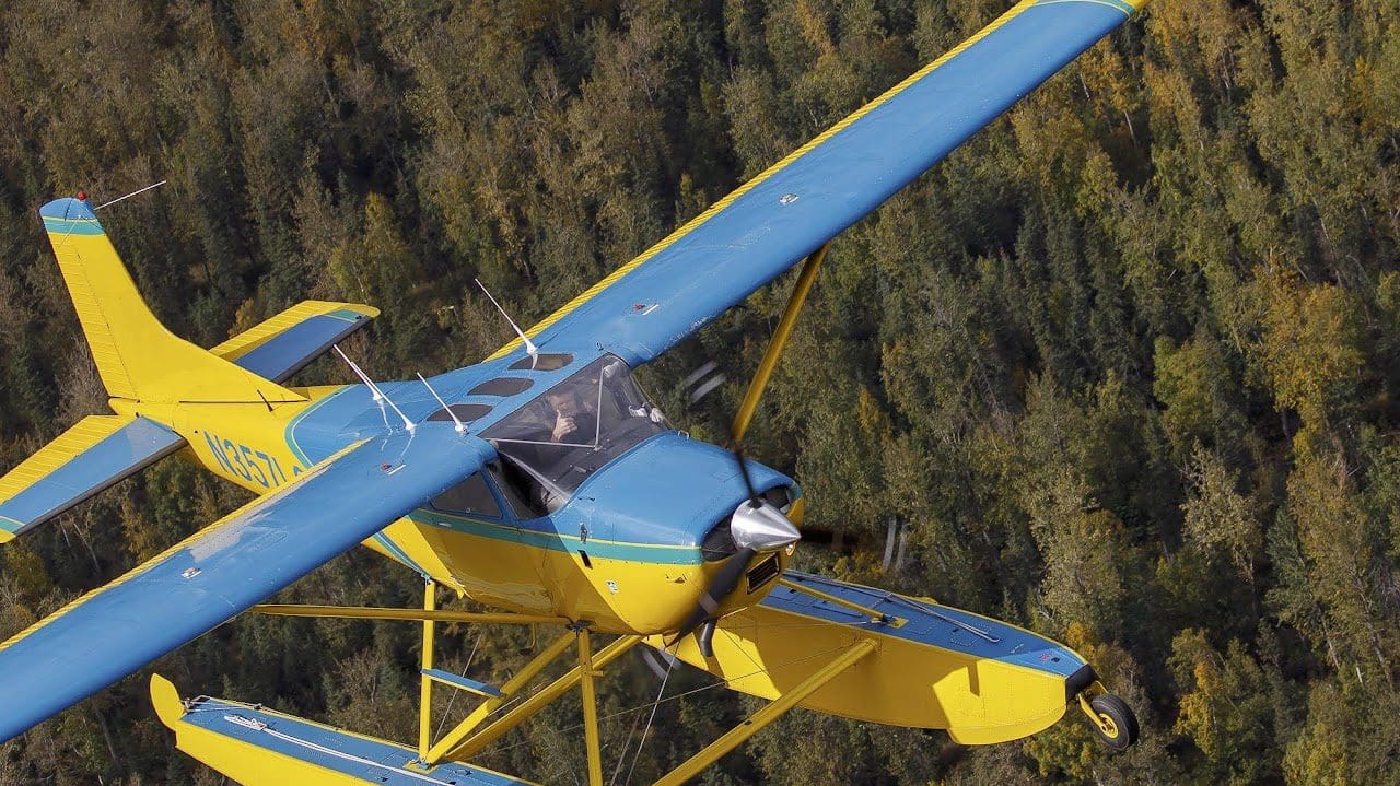 Yellow and blue seaplane flying over forest.