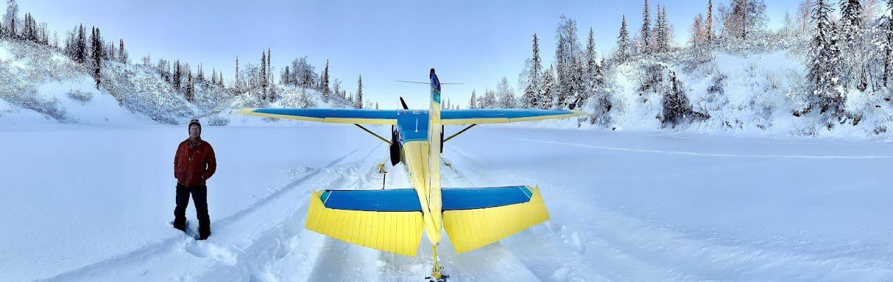 Yellow airplane on snowy landscape, person nearby.