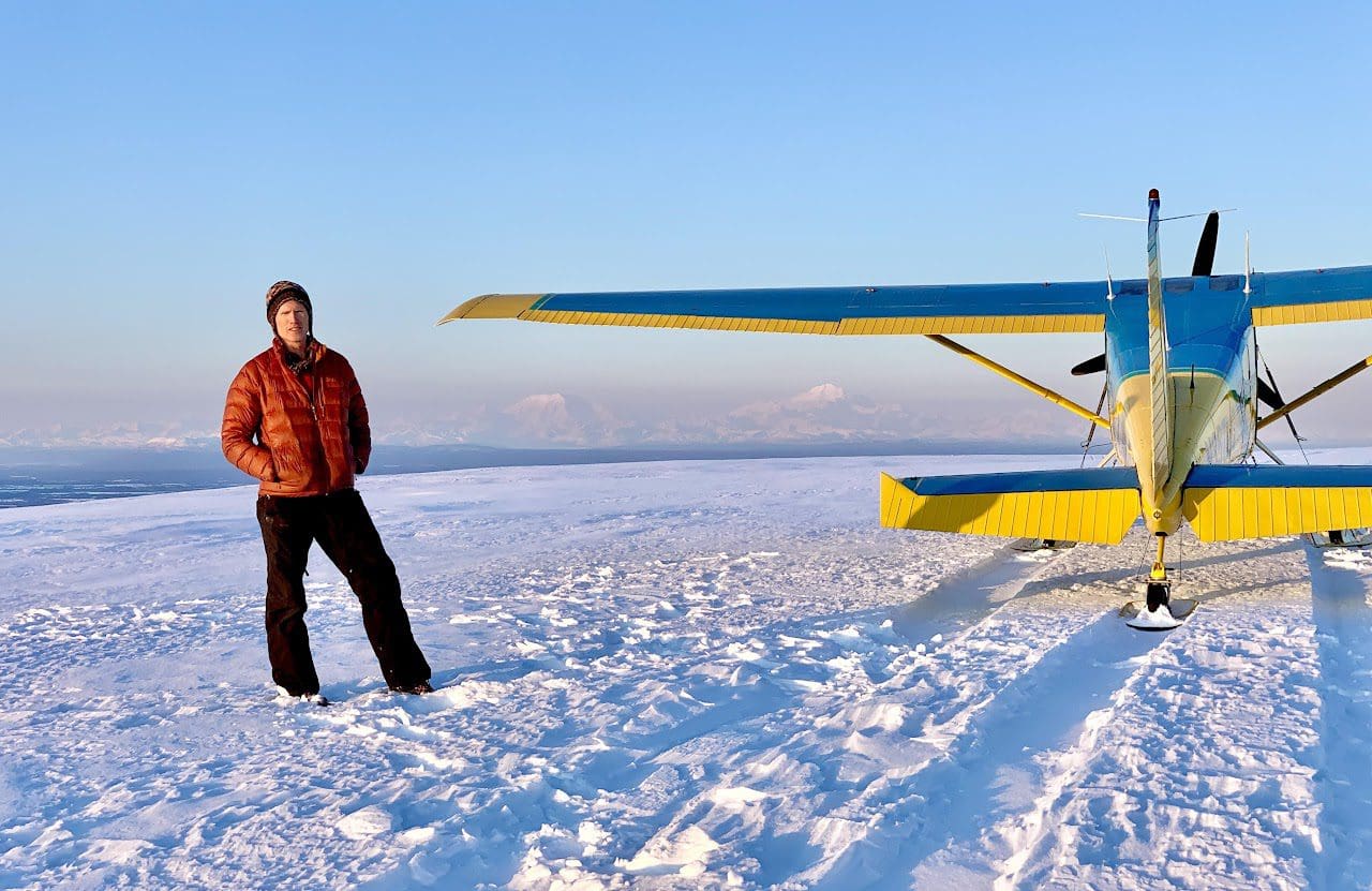 Person standing beside small airplane on snow.