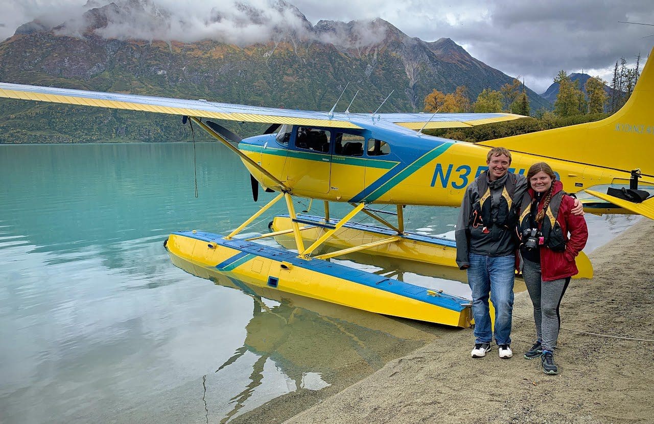 Couple standing by yellow seaplane on lake.