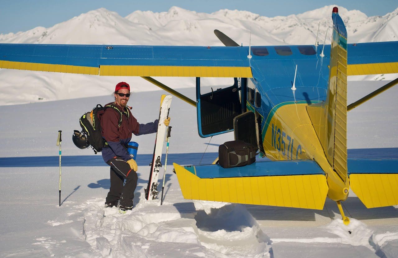 Man with skis beside small plane on snow.
