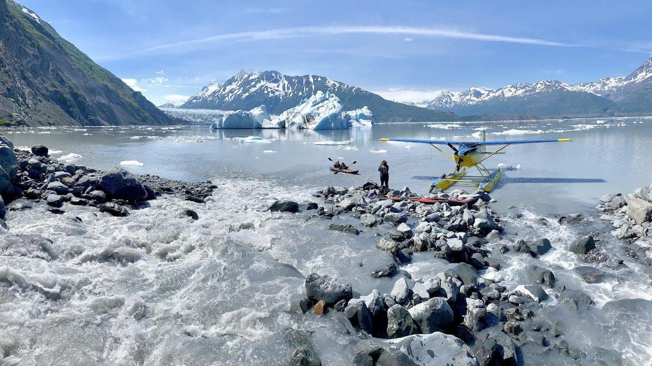 Seaplane by icy lake and snowy mountains.