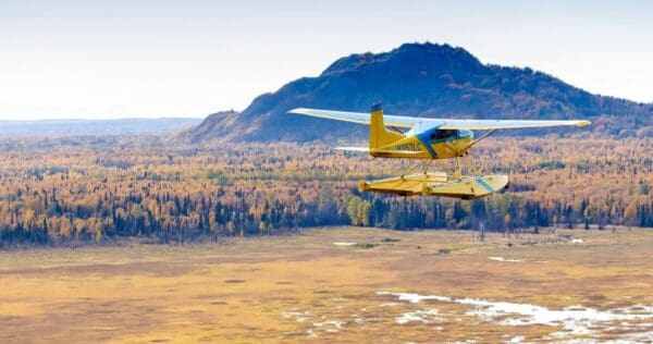 Yellow seaplane flying over autumn landscape.