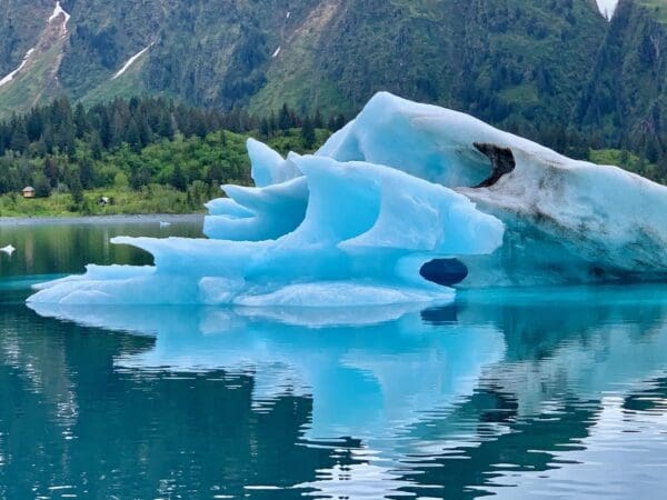 Blue iceberg reflecting in calm lake water.