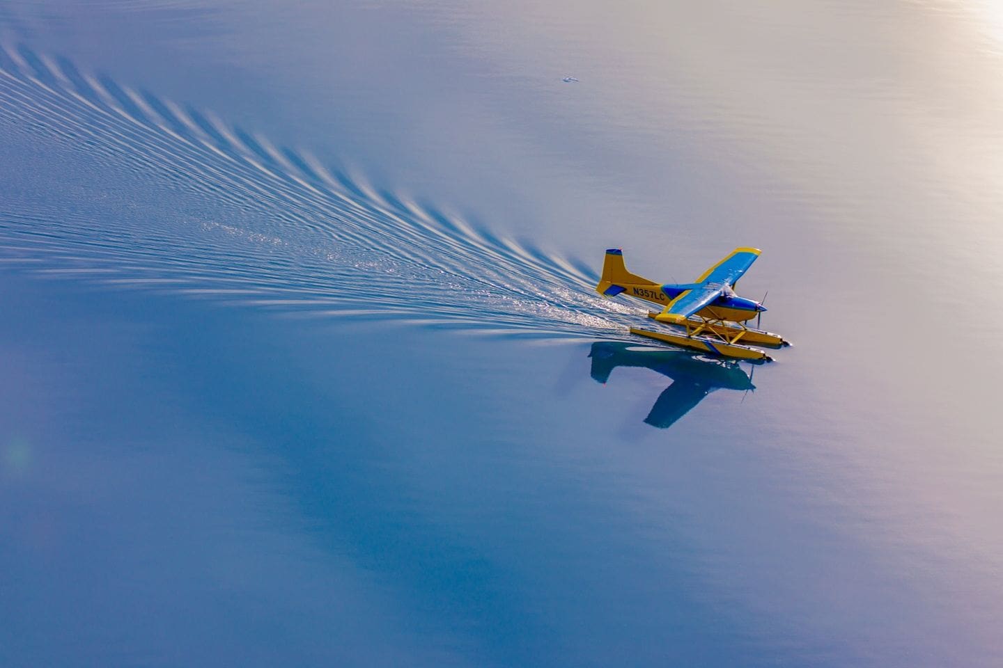 Yellow seaplane gliding on calm blue water.