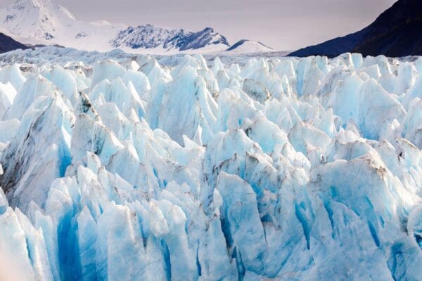 Blue glacier with snowy mountains in background.
