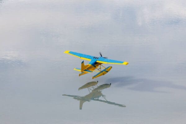 Blue-yellow seaplane flying over calm water.