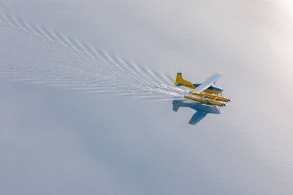 Yellow seaplane gliding on calm water.