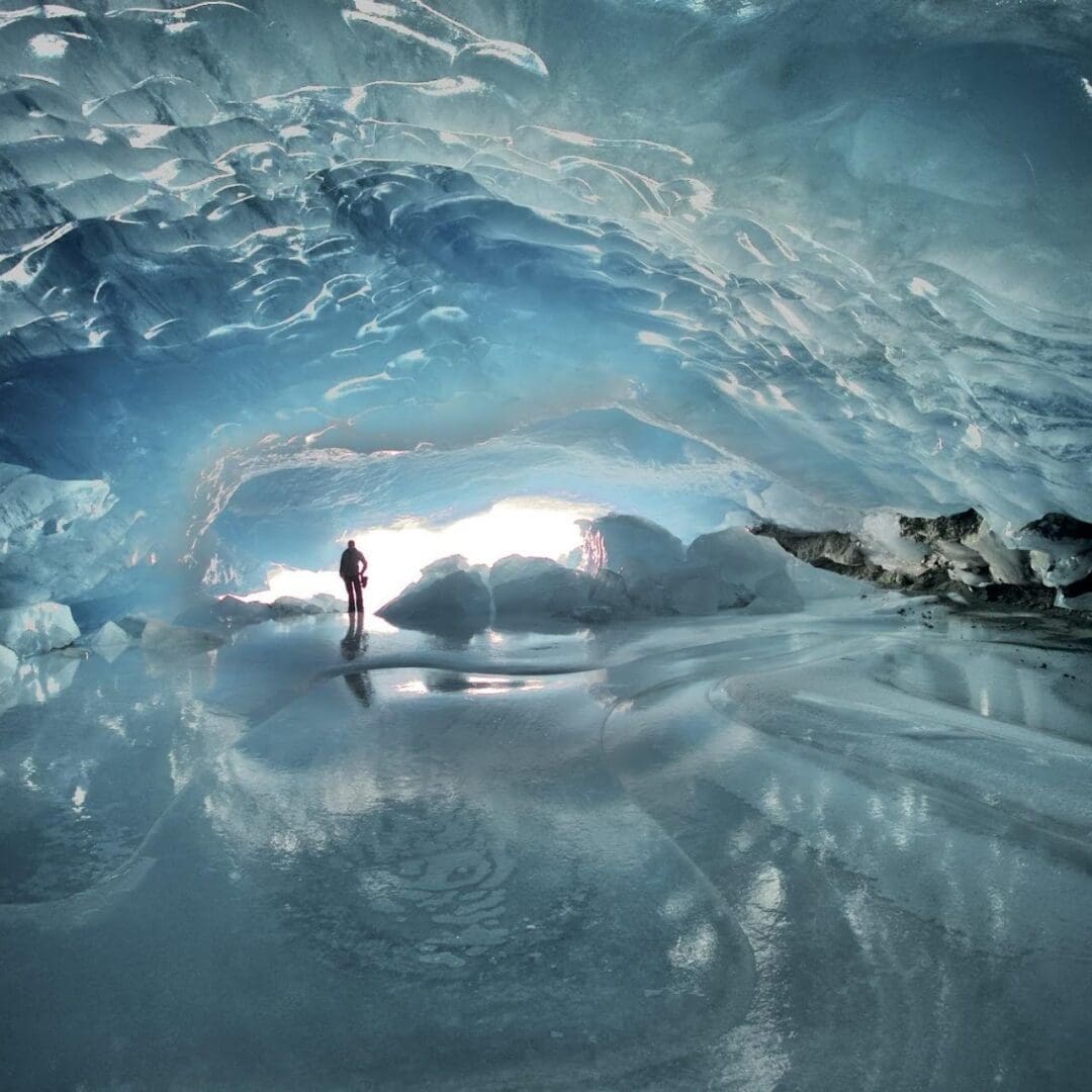 Person standing inside a blue ice cave.